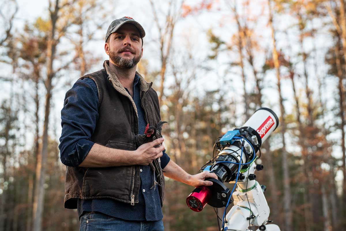 Brennan Gilmore standing next to a powerful telescope surrounded by trees