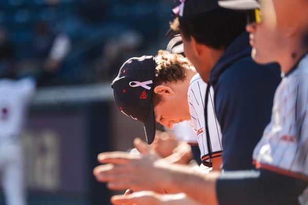 A UVA baseball player lowers his head revealing the purple ribbon on his cap