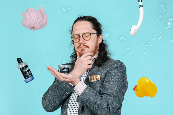 Zachary Irving looks at a &quot;Lush&quot; product with a pensive expression while other shower items hang in the air around him