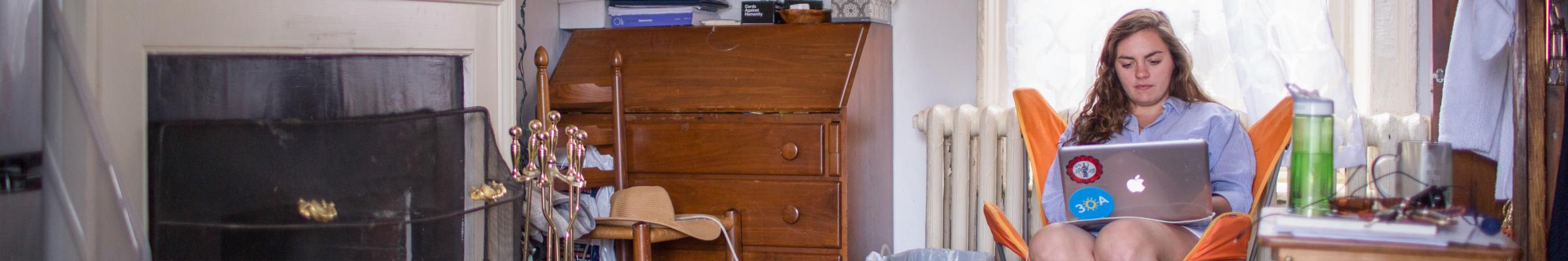 A banner portrait of a girl working on her laptop in her dorm room.